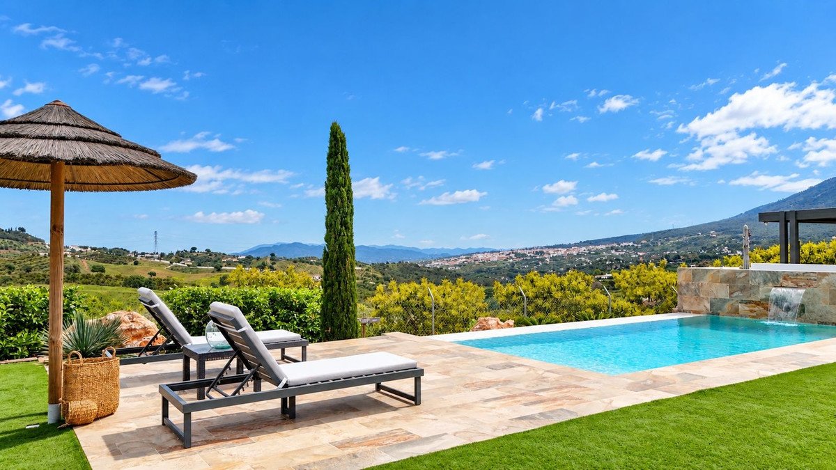 Luxury swimming pool with waterfall feature and sun loungers, offering stunning panoramic views of the rolling hills and distant town.