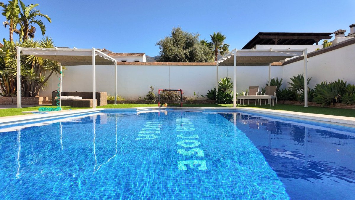 A bright blue swimming pool with the name 'Maria Jose Lucia' inscribed on the bottom. Two shaded seating areas are visible with furniture.