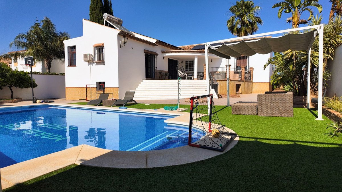 Villa with a large swimming pool, artificial turf, basketball hoop, and soccer goal under a sunny sky.