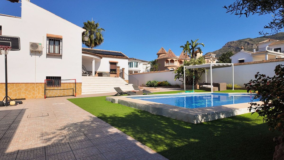 Villa with a swimming pool, lounge chairs, a basketball hoop, and a soccer goal, set against a backdrop of hills.