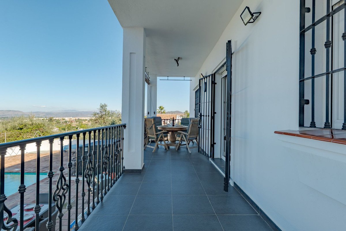 Covered balcony with pool and mountain views, wooden table, black railings, and tiled floor.