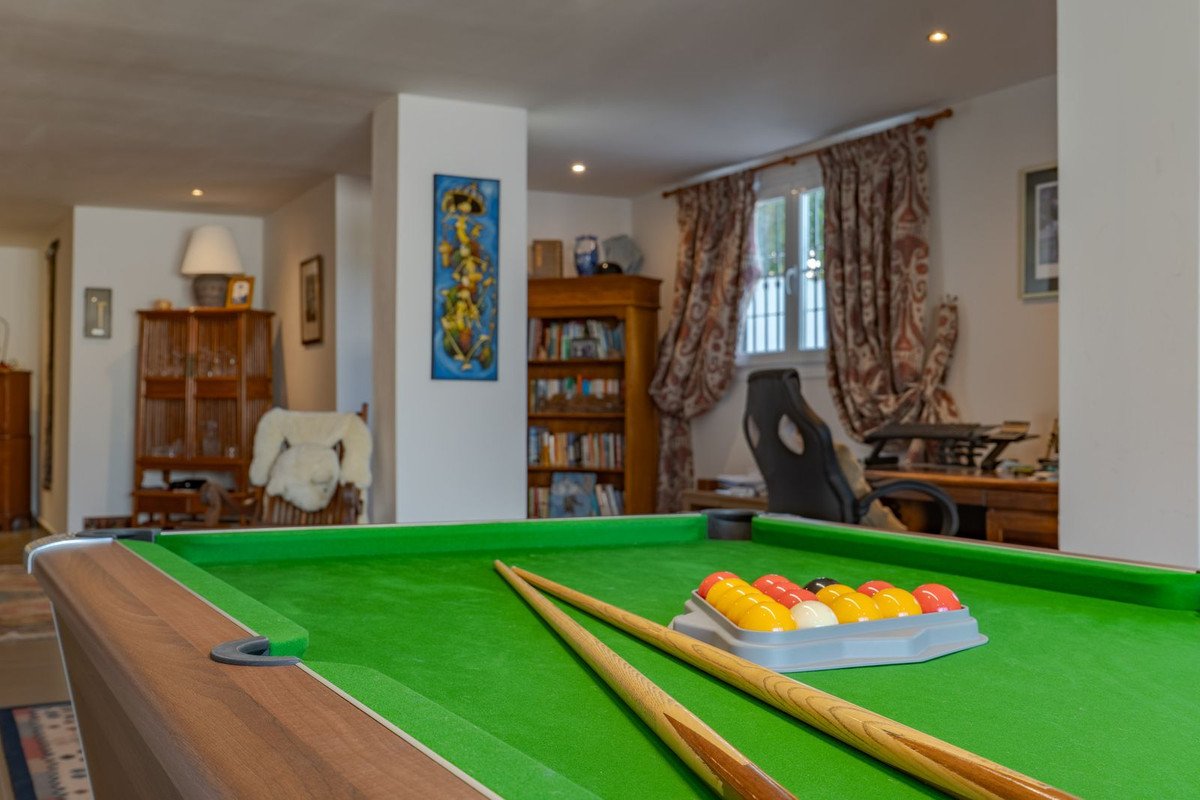 Well-lit living room featuring a pool table with cues and balls, bookshelves, and a window with curtains