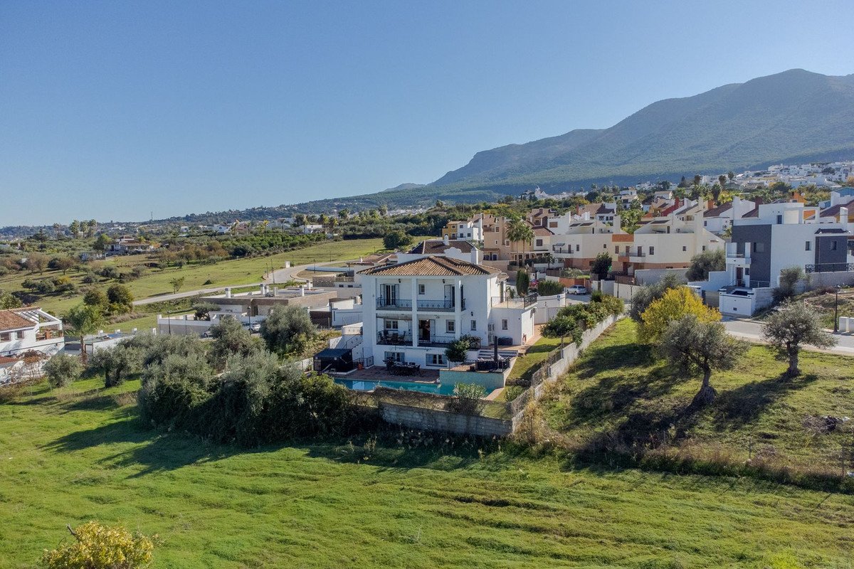 Villa with pool, garden, and mountain views in a sunny, green landscape.