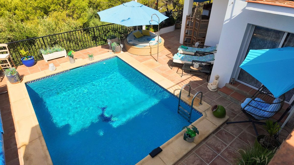 A private swimming pool and terrace with sun loungers, outdoor seating, and umbrellas, surrounded by lush greenery.