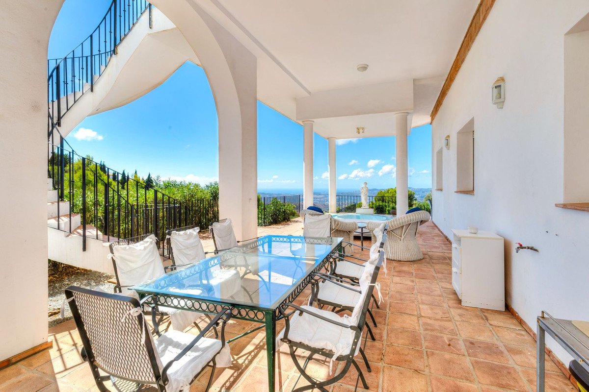 Covered terrace with dining table and chairs, overlooking the sea. Features a spiral staircase and fountain.