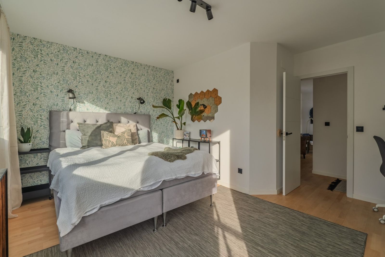 Stijlvolle slaapkamer met bloemenbehang en grijs bed.