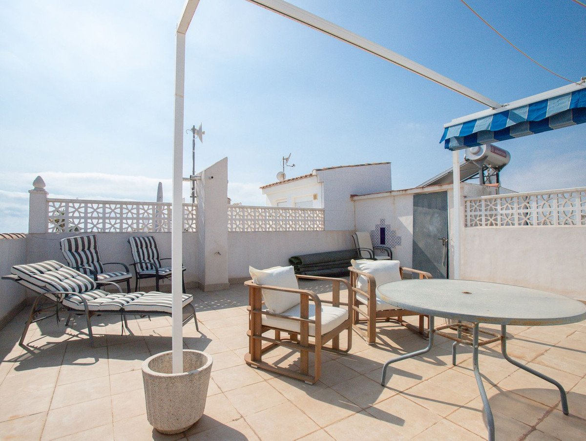 A sunny terrace with lounge chairs, seating area, and dining table under a blue and white awning.