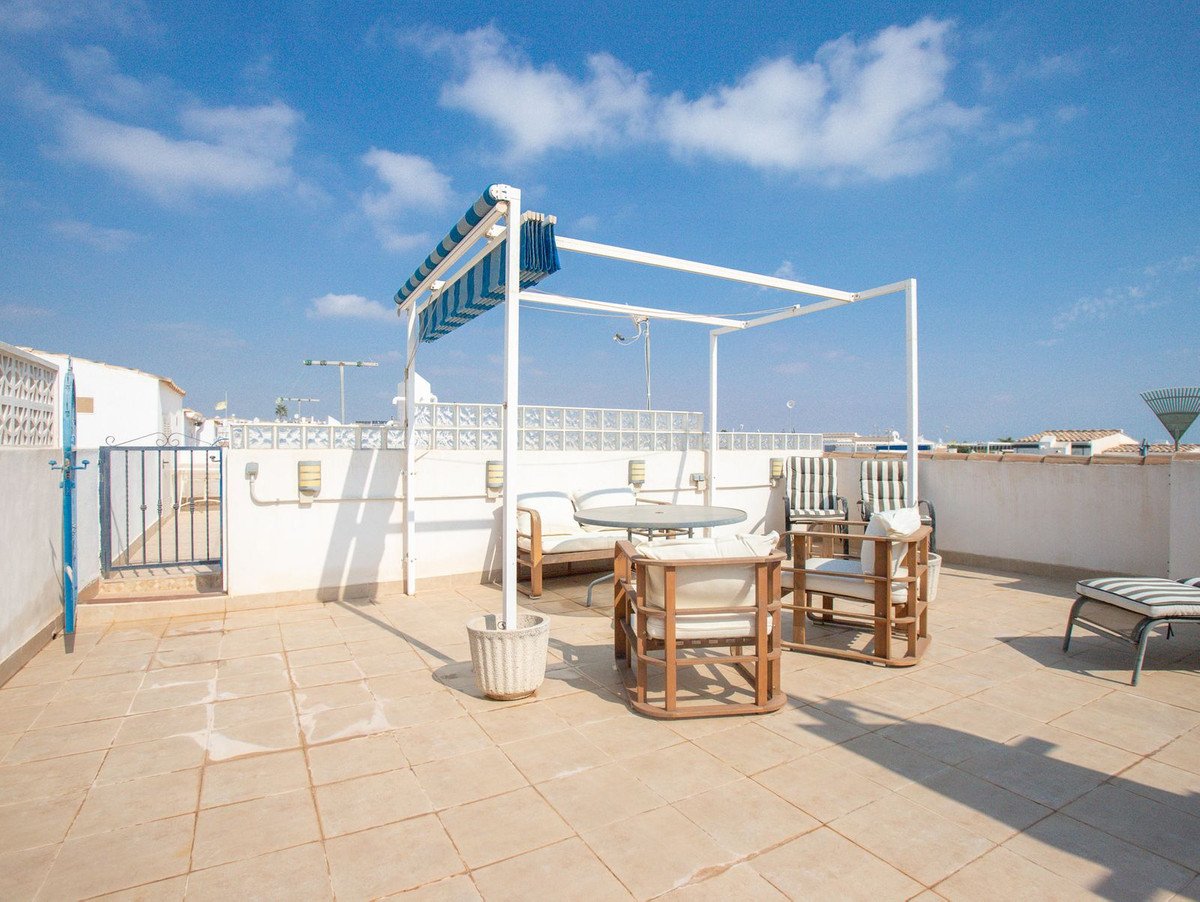 A tiled terrace with outdoor seating, a table, and a pergola under a blue sky.