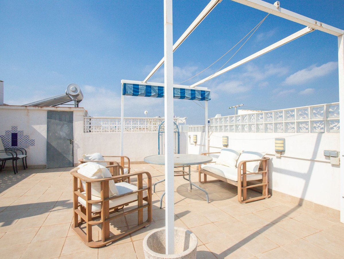 Outdoor terrace with wooden seating, table, and blue striped awning under a clear blue sky.