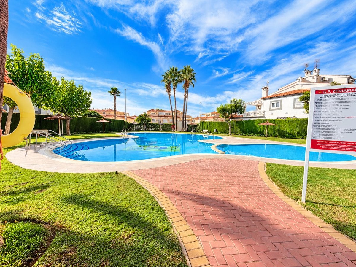 A bright blue communal swimming pool with palm trees and residential buildings in the background under a sunny sky.