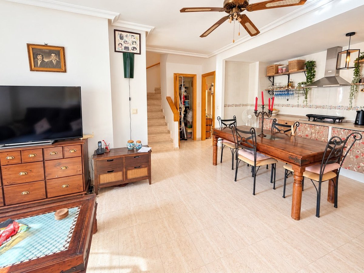 Spacious open-plan living, dining, and kitchen area with wooden furniture and ceiling fan.