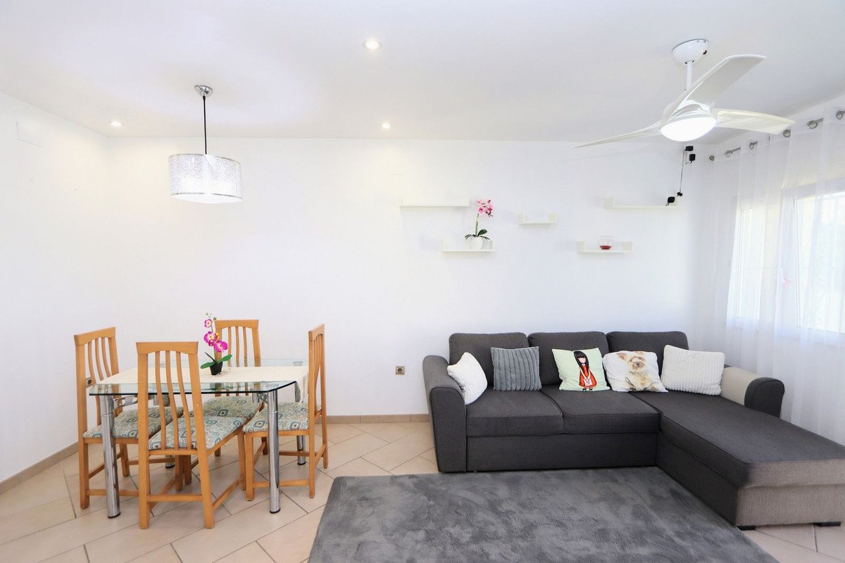 A bright living and dining area with a sectional sofa, glass dining table, and a ceiling fan.