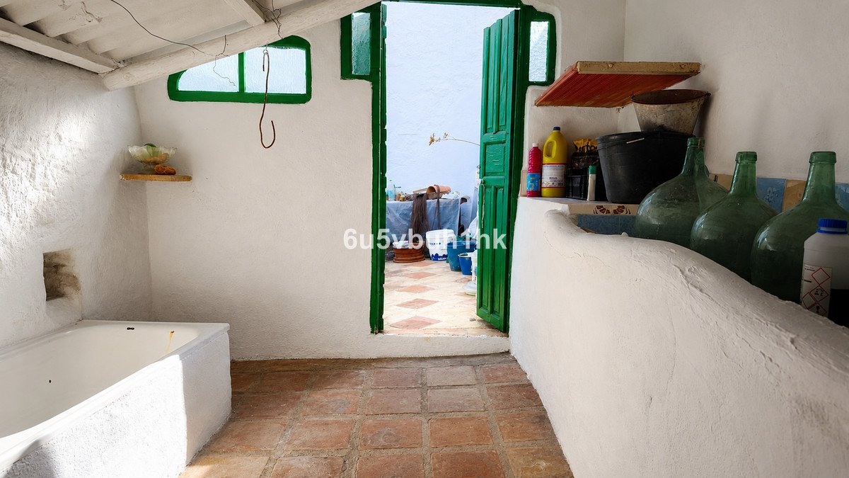 A white bathtub in a room with terracotta tiles and a green door opening to a sunny terrace with a view.