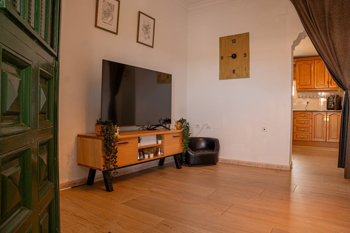 Living room with a large TV on a wooden cabinet, a small black chair, and a view into the kitchen.