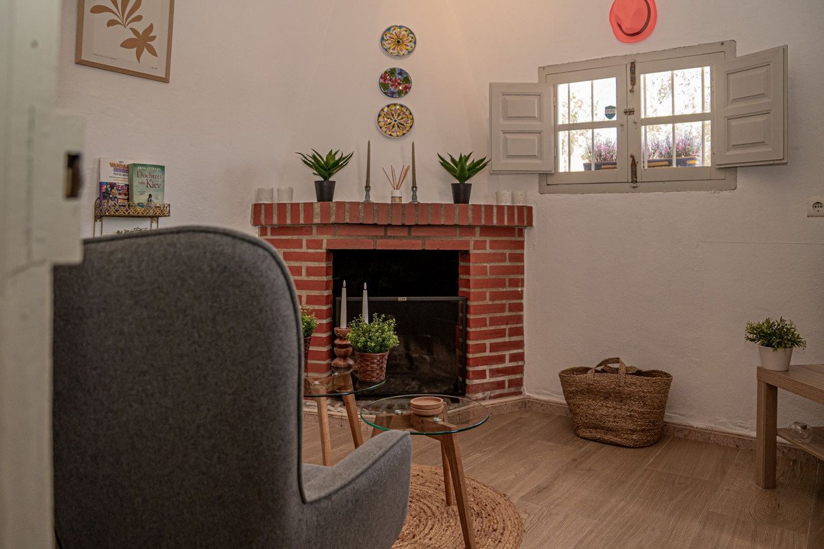 Cozy living room with a red brick fireplace, comfortable armchair, and a window with shutters overlooking lavender plants.