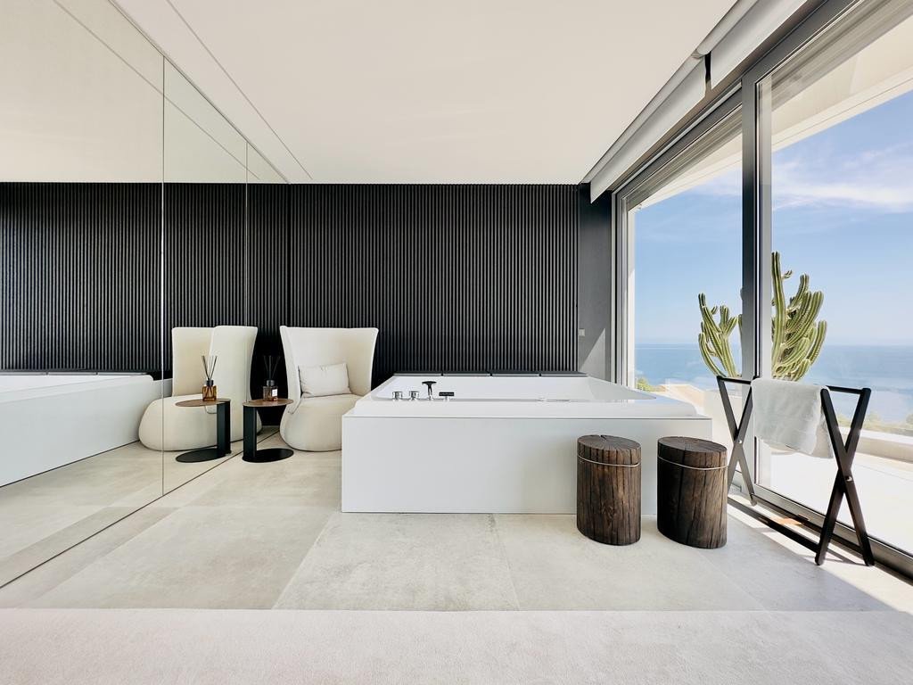 Modern bathroom with sea view, white tub, and large windows