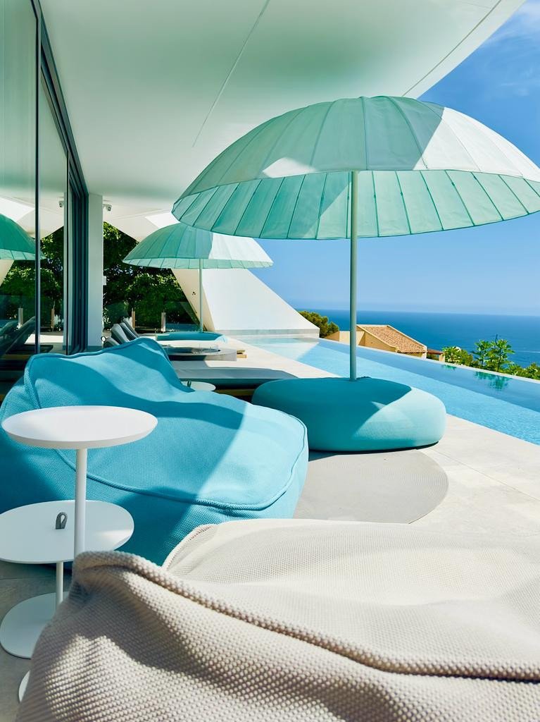 Modern patio with blue lounge chairs, umbrellas, and ocean view.