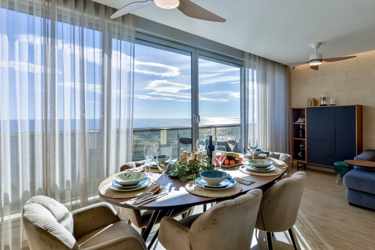 Dining area with a table set for a meal, overlooking the ocean through large windows and a balcony.
