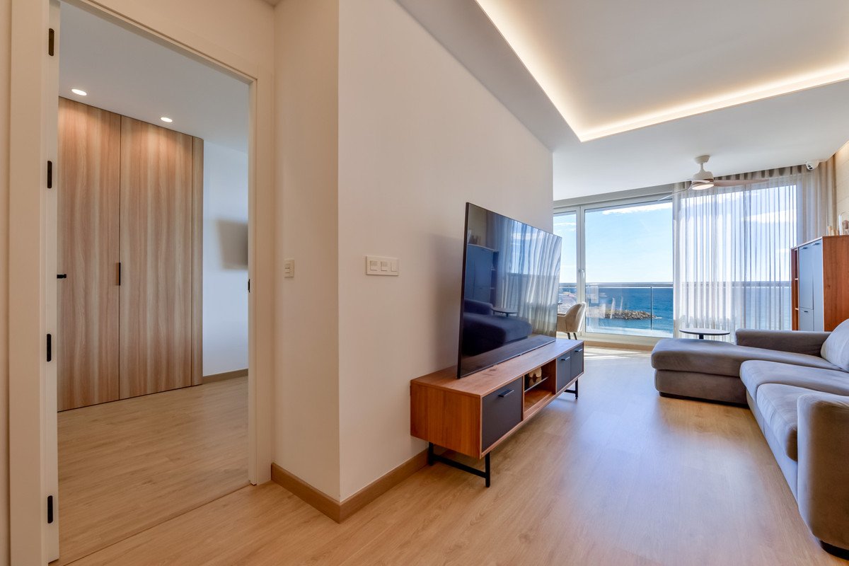 Modern living room with large windows, a grey sofa, and a stunning sea view. Features modern entertainment unit and cabinets.