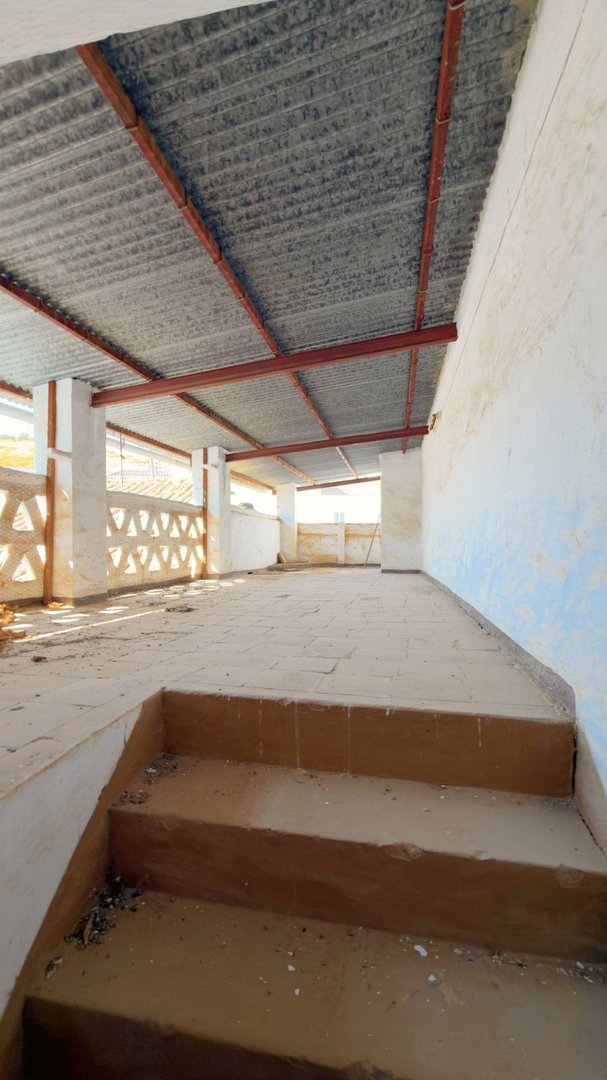 A partially constructed outdoor covered terrace area with a metal roof and decorative concrete block walls. Shows steps leading up to the space.