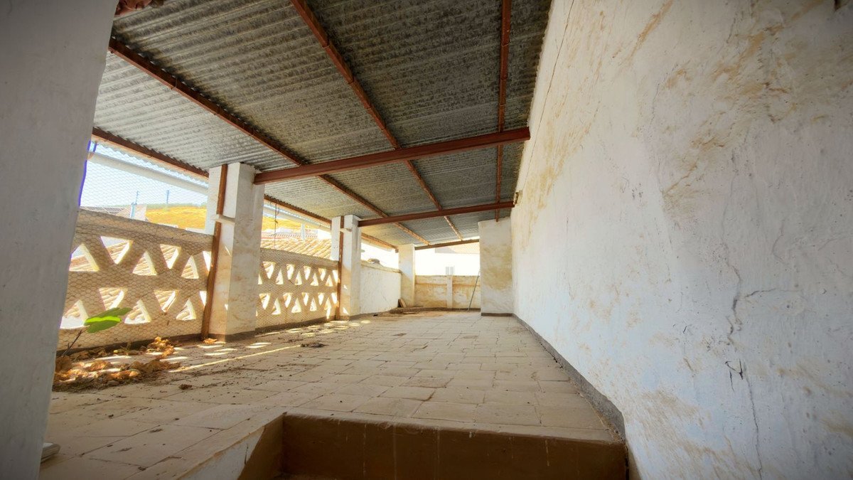 A covered terrace with tiled floor, decorative patterned walls and a corrugated metal roof.