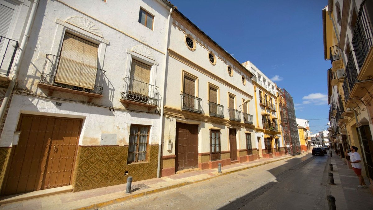 Traditional Spanish townhouse with balconies and brown wooden doors lining a sunny street.