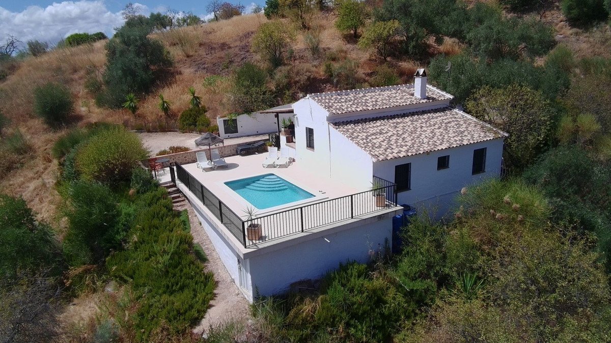 A white villa with a swimming pool and sun loungers on a terrace, surrounded by lush greenery.