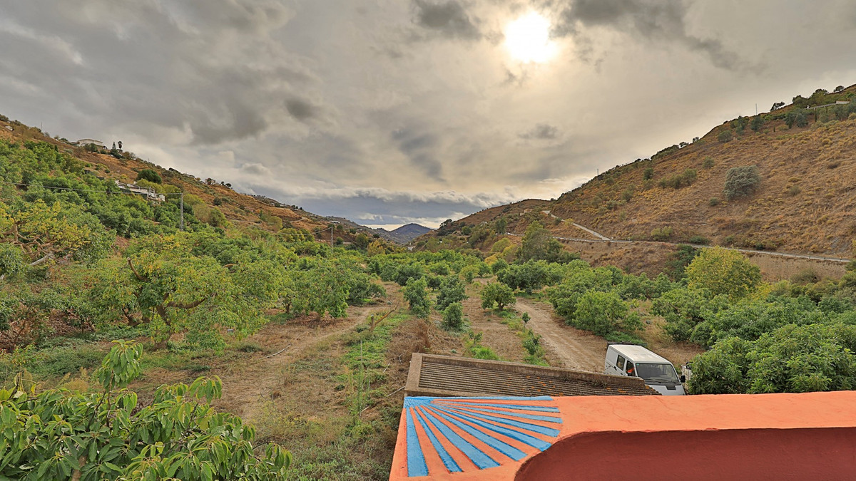 Uitzicht op een bergdal met bomen, een huis, een auto en bewolkte lucht.