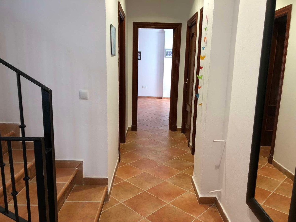 Hal met trap, terracotta vloertegels en houten deuren.