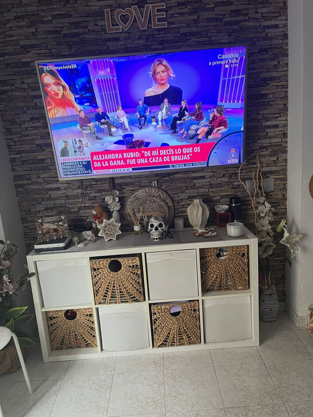 Televisie boven witte kast met decoraties en rieten manden.