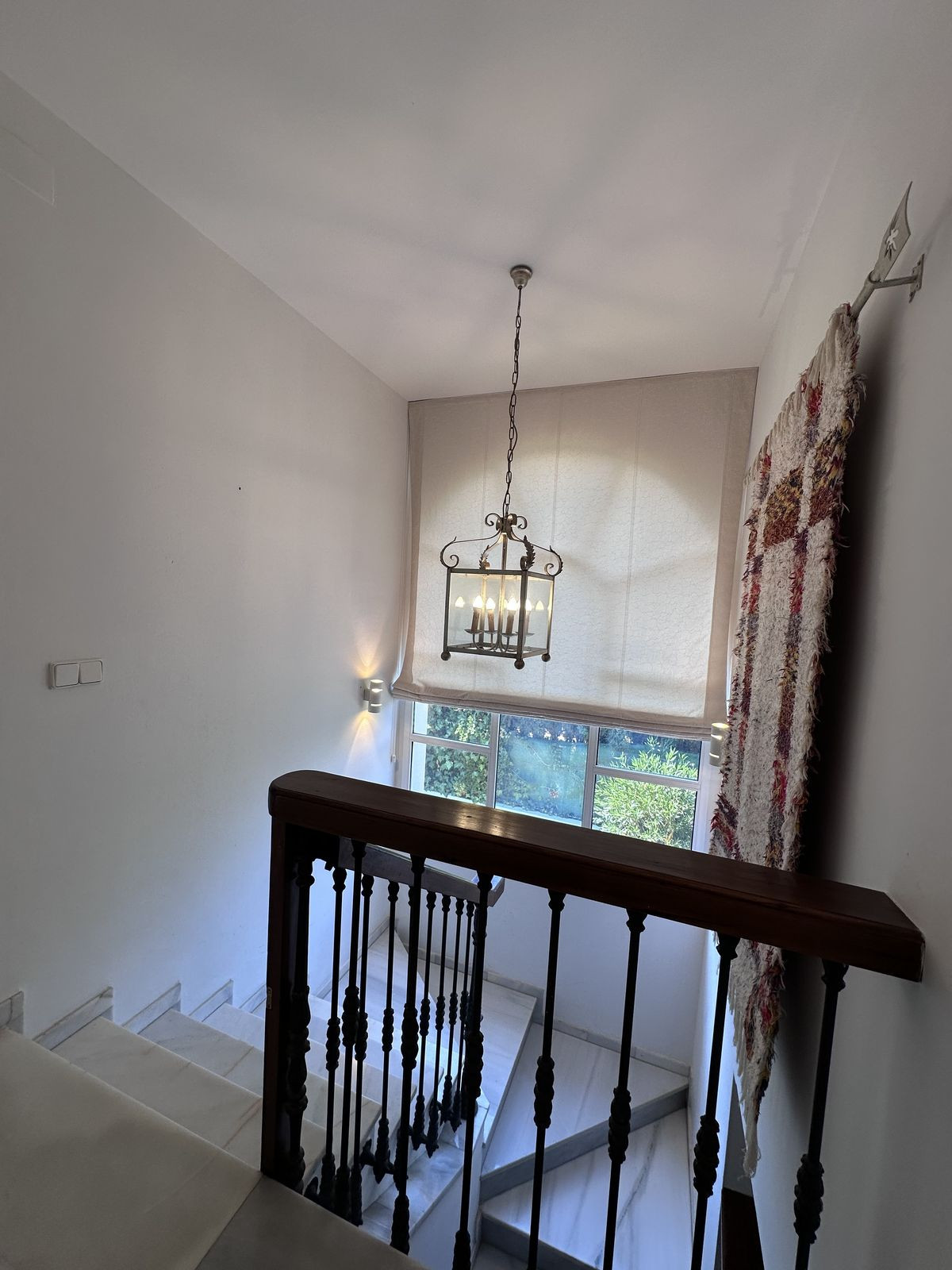 Trapopgang met kroonluchter en raam met uitzicht op groen.