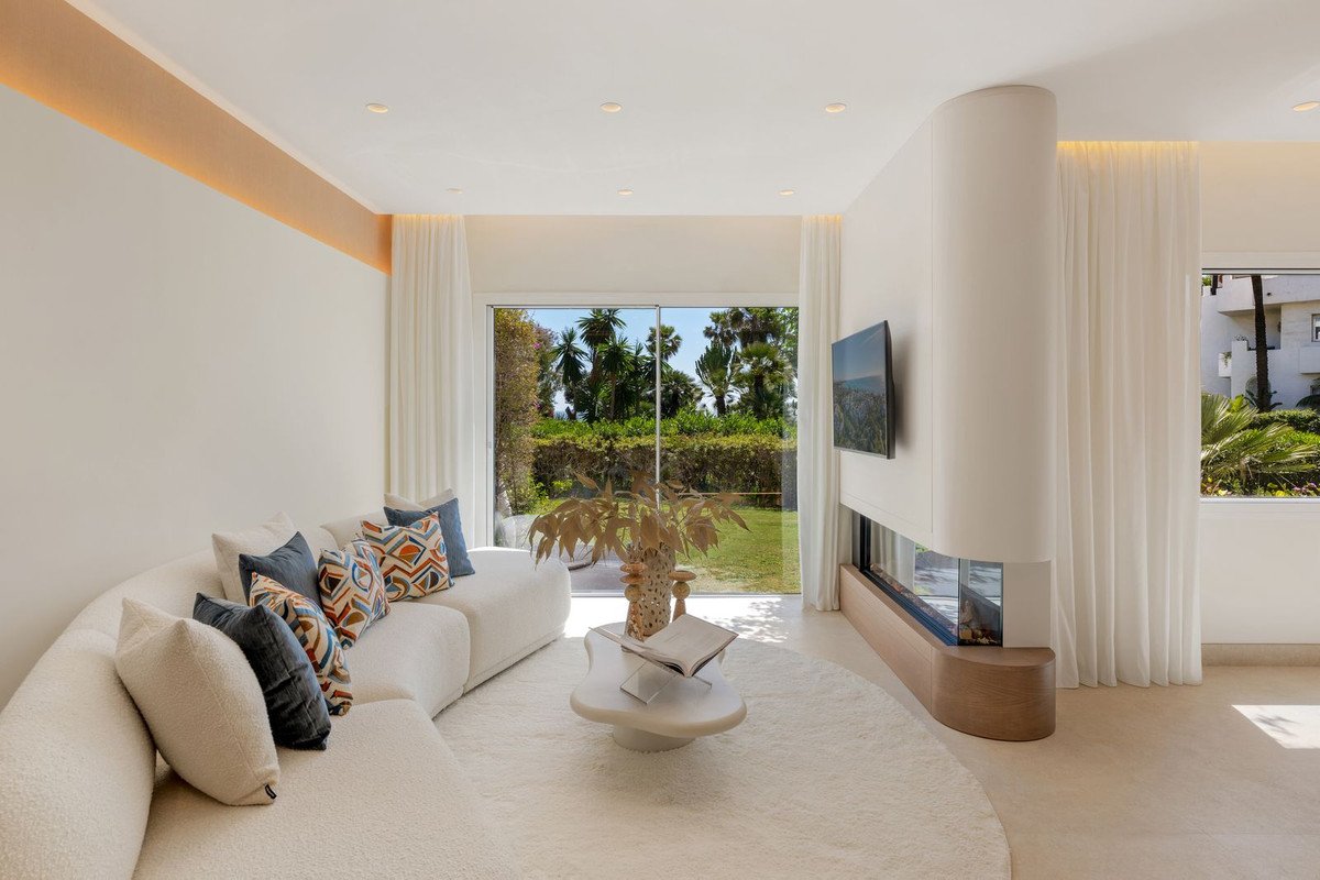 Modern living room with a large sectional sofa, fireplace, TV, and expansive glass doors opening to a lush garden view.