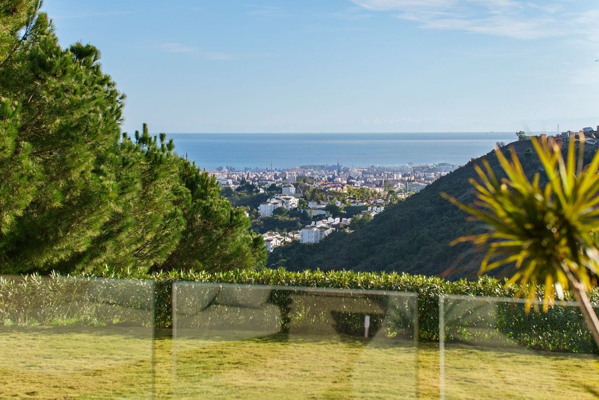 Terrace with sea and town view, surrounded by green trees and lawn. Clear blue sky above.