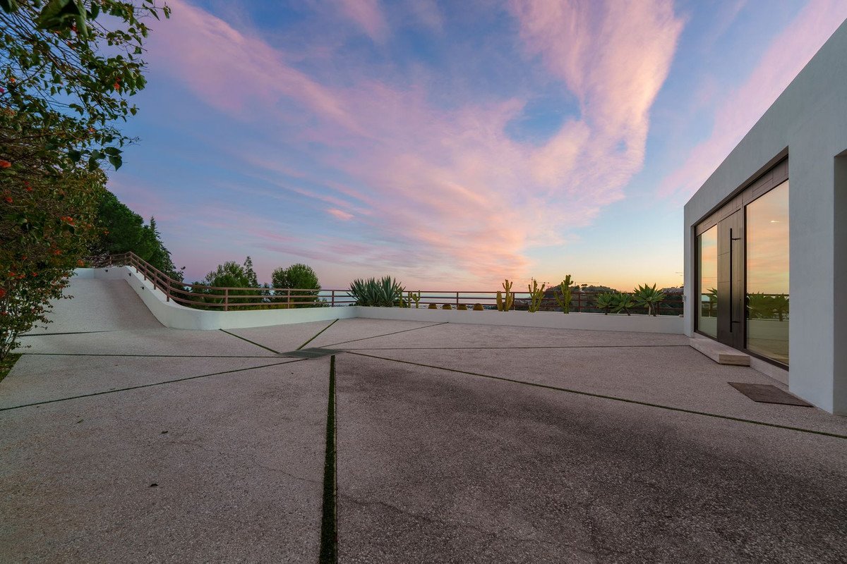 Modern home driveway and entrance with large glass doors, overlooking a scenic sunset with colorful clouds.