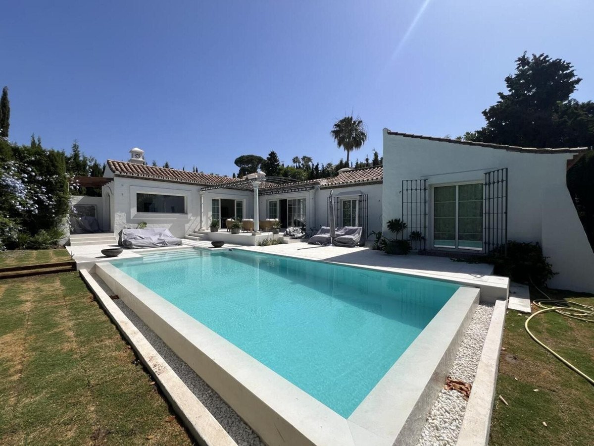 A white villa with a large blue swimming pool and a patio with lounge chairs.