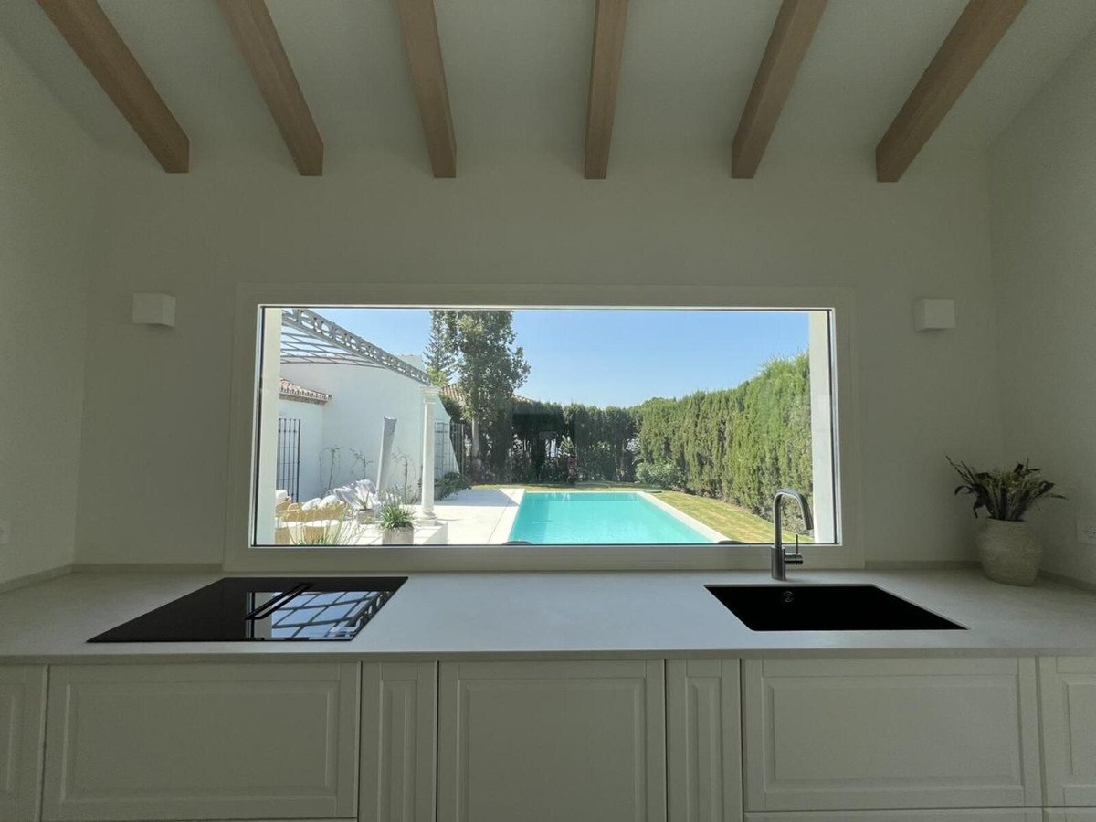 Modern kitchen with sink and stove overlooking a swimming pool and lush garden on a sunny day.