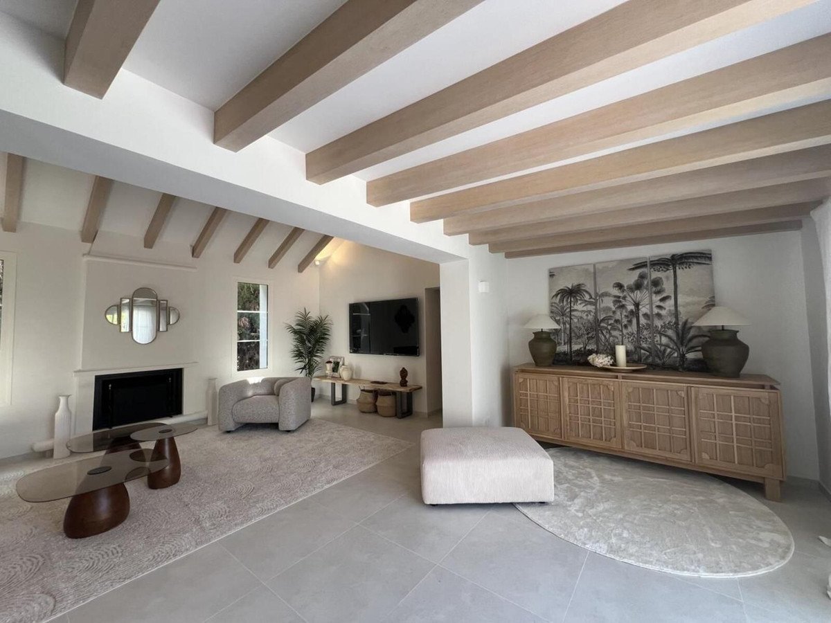 Modern living room with exposed wooden ceiling beams, fireplace, large console, and artwork.