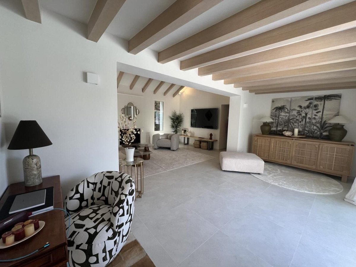 Modern living room with exposed wooden beams, minimalist furniture, and tropical wall art.