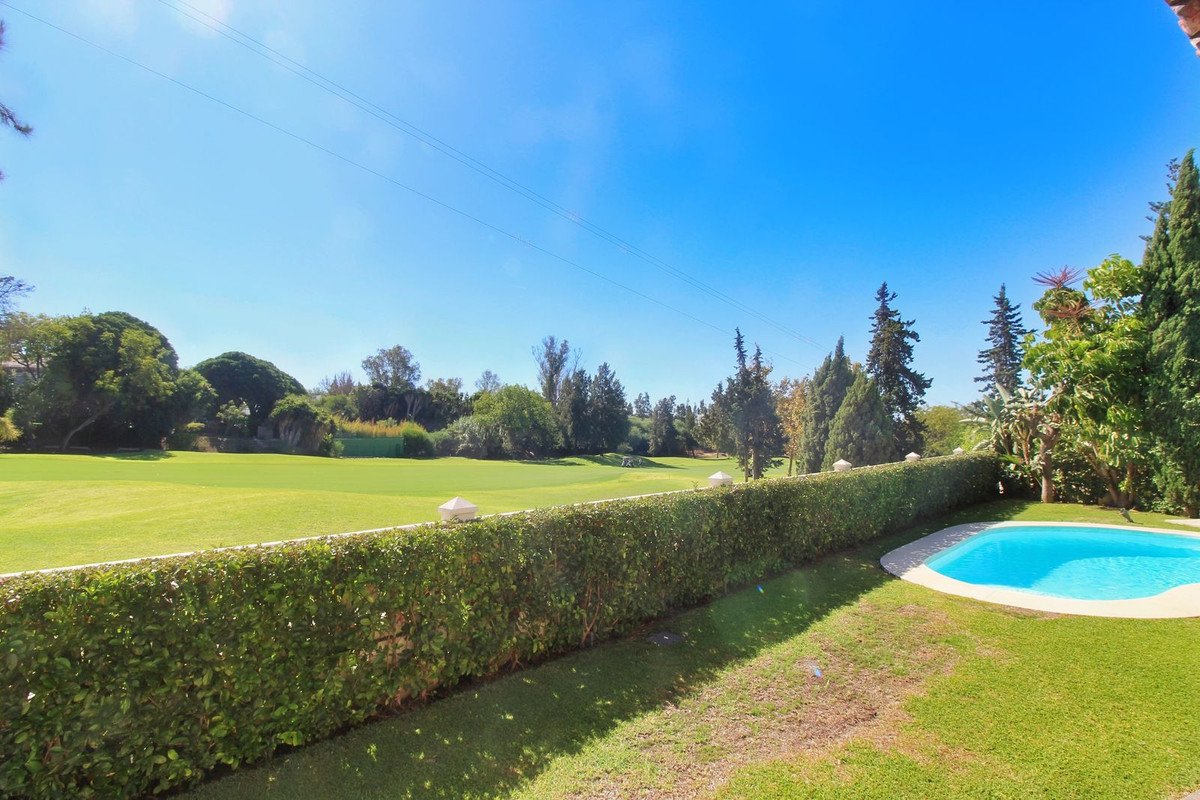 A garden with a swimming pool and a hedge overlooking a lush green golf course under a bright blue sky.