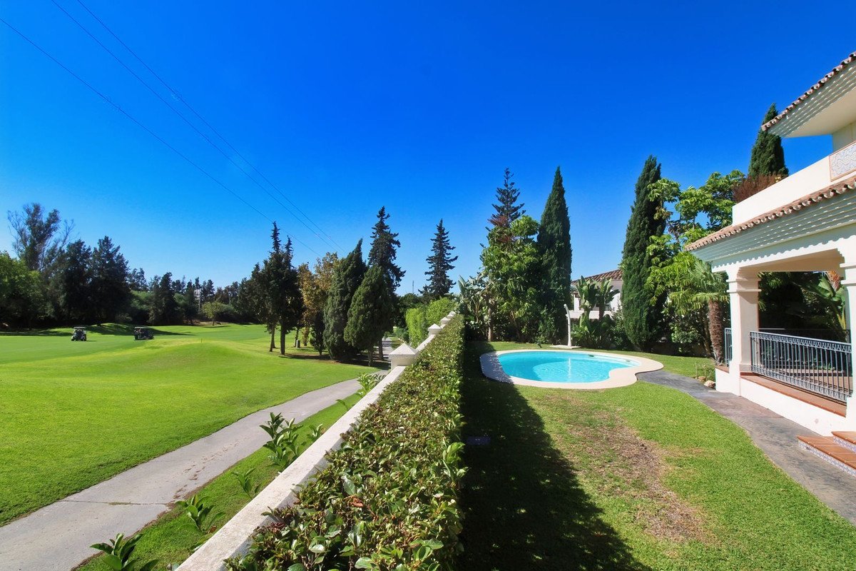 View from property balcony overlooking a swimming pool, garden, and a lush golf course with golf carts.