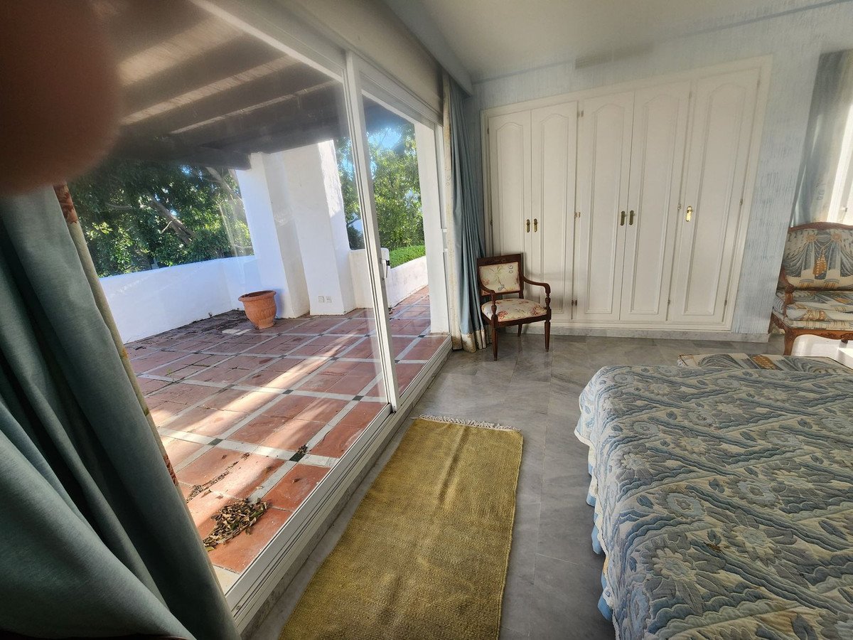 Bedroom with large white wardrobe, blue bedspread, and sliding doors opening to a tiled terrace with greenery beyond.
