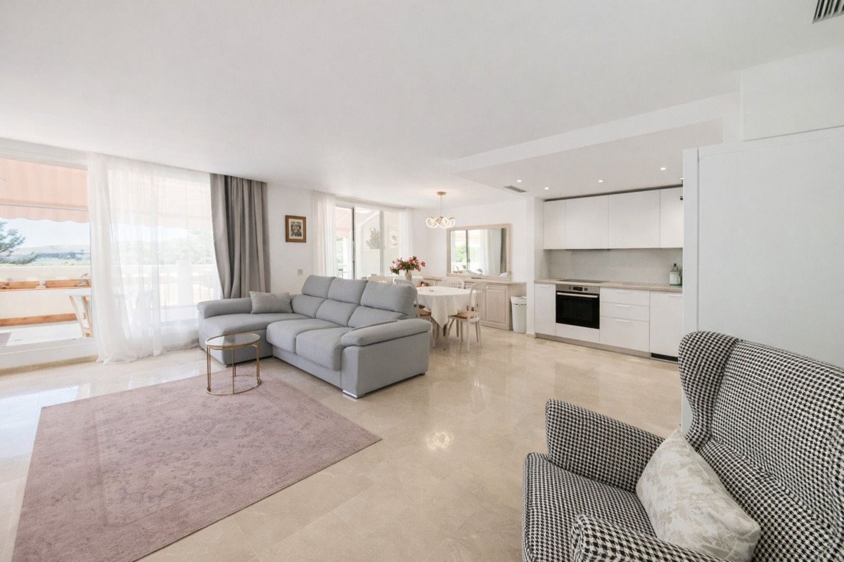 Modern open-plan living, dining, and kitchen area with a large sectional sofa, dining table, and balcony access.
