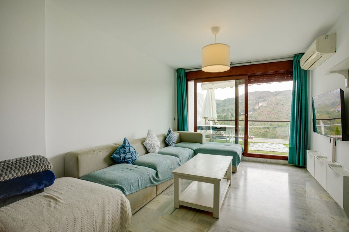 Modern living room with sofa, coffee table, TV, and balcony view of hills.