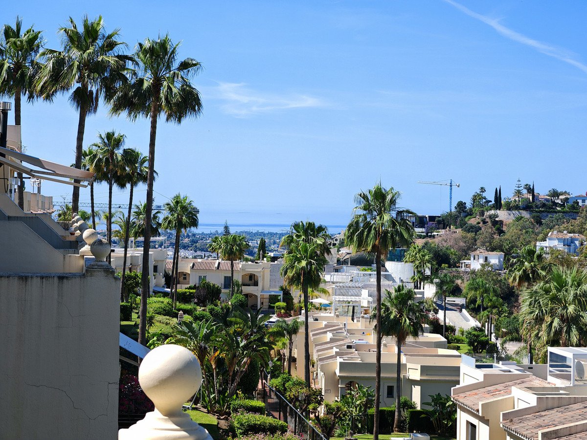 Sea view from balcony with palm trees and resort buildings under blue sky.