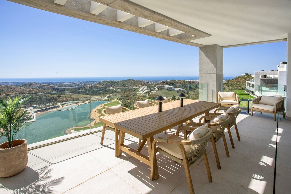Modern balcony with dining table, ocean and golf course views, glass railings, and potted plant.