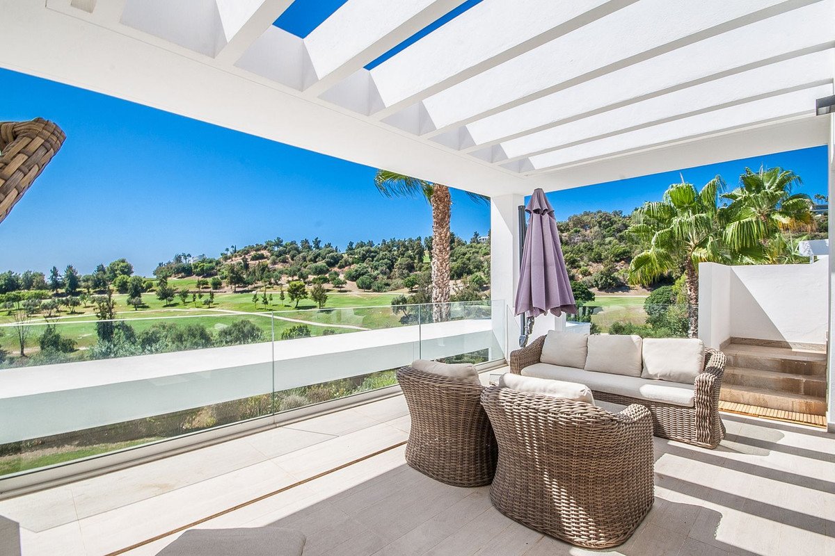 A covered terrace with outdoor seating overlooks a lush green golf course under a clear blue sky.