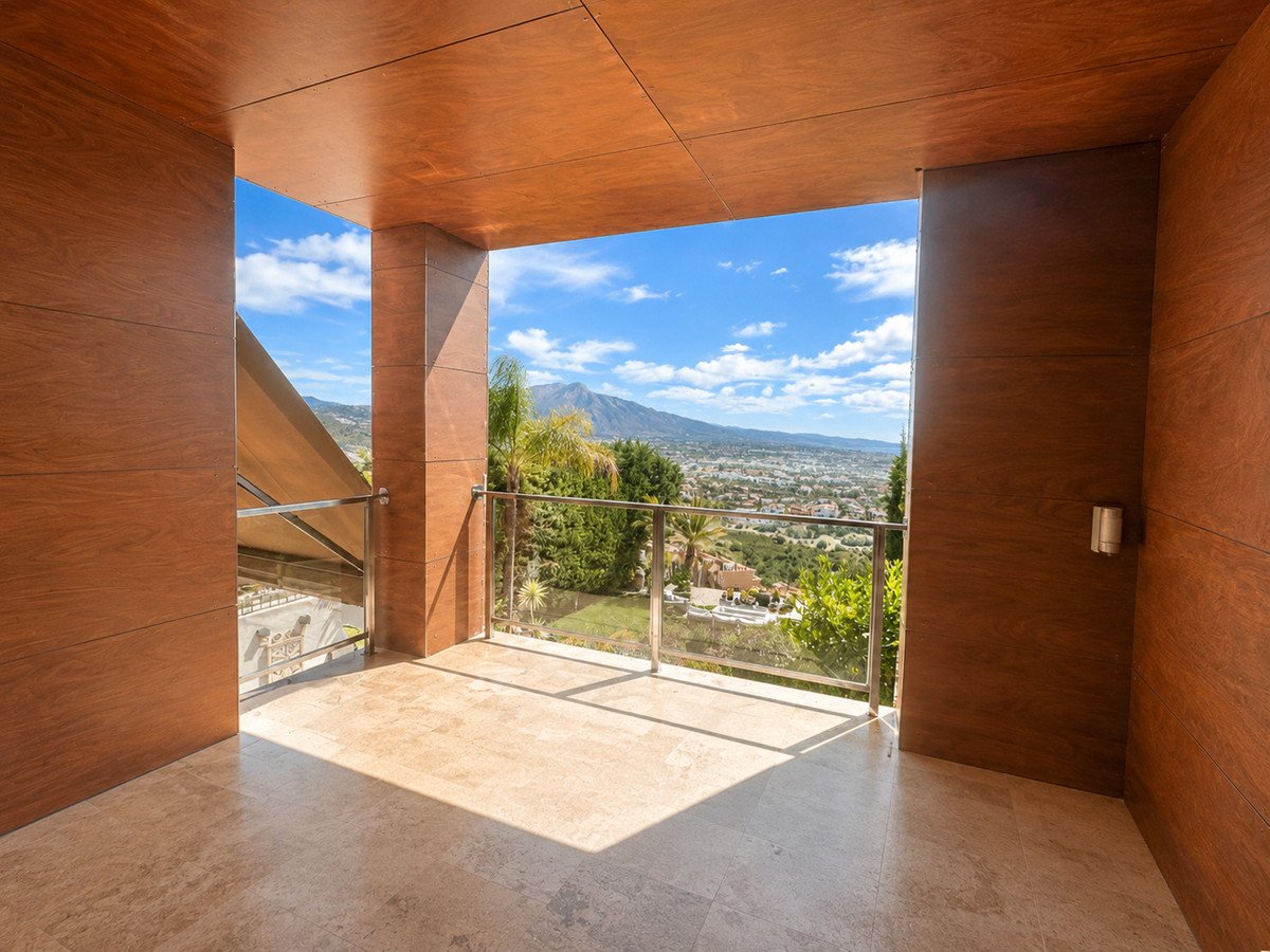 Modern balcony with wood walls, tiled floor, glass railing, and panoramic mountain and city views.