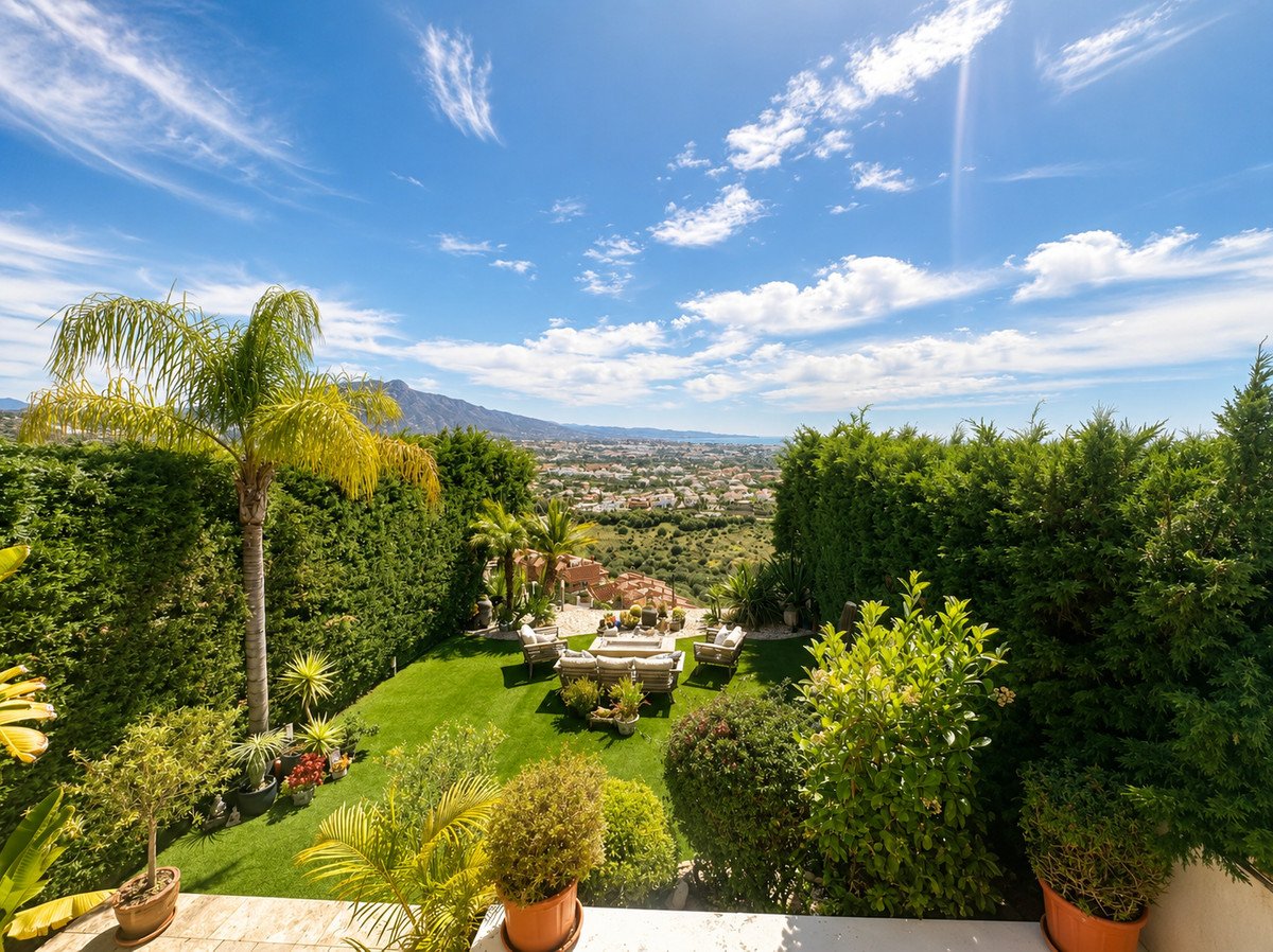 Lush garden with palm trees, outdoor seating, and panoramic mountain and city views under a blue sky.