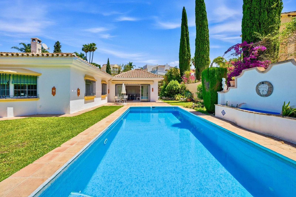 A spacious villa with a private swimming pool, lush green lawn, and beautiful garden on a sunny day.