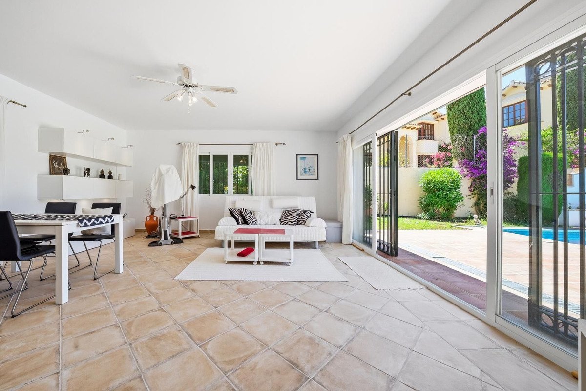 Bright living and dining area with sliding doors opening to a sunny garden with a swimming pool.